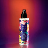 Flacon spray de la brume corps parfumée hydratante Minuit Chéri à l’extrait de ginseng, sur fond dégradé violet et orangé.