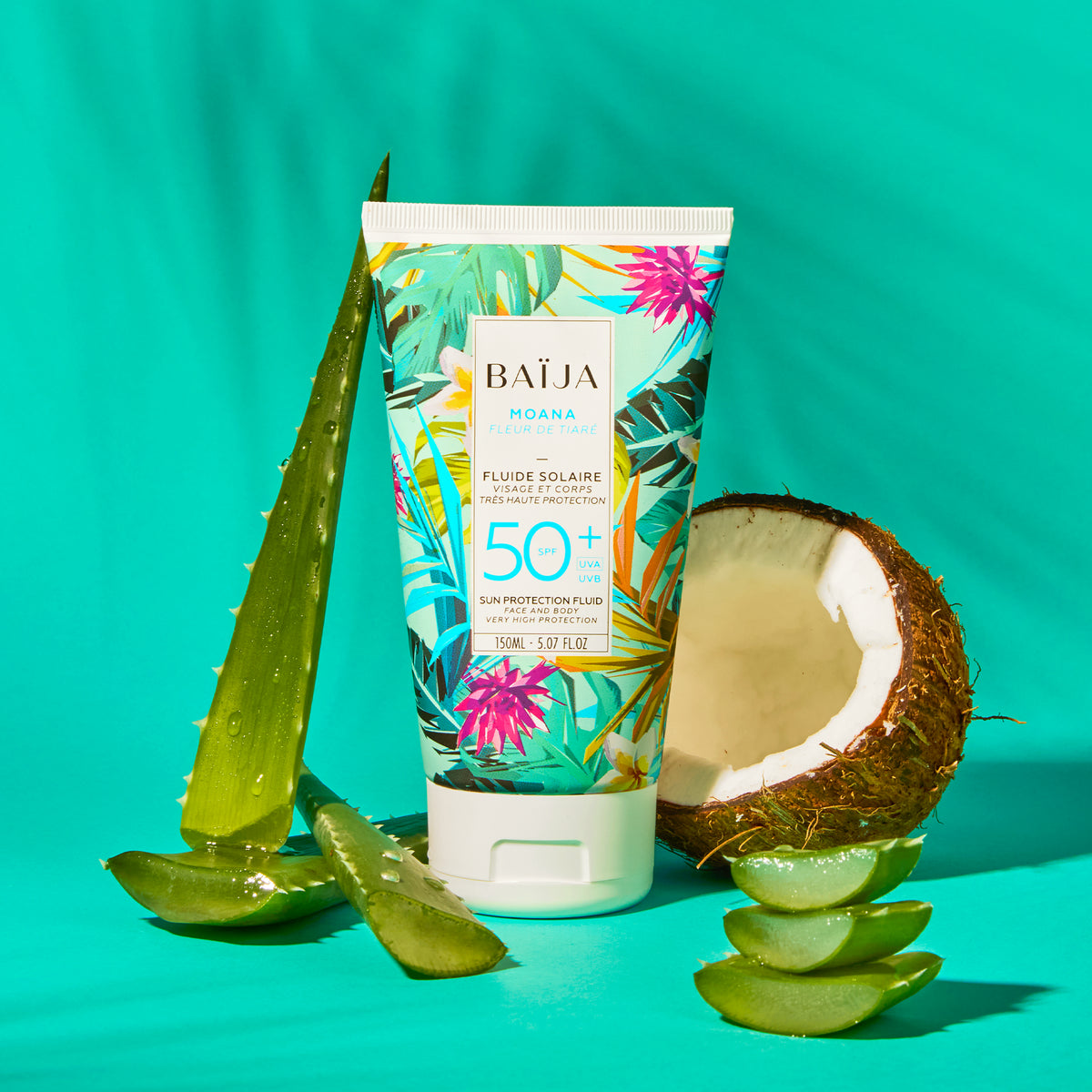 Fluide solaire Moana SPF 50+ posé entre aloe vera et noix de coco sur fond turquoise.