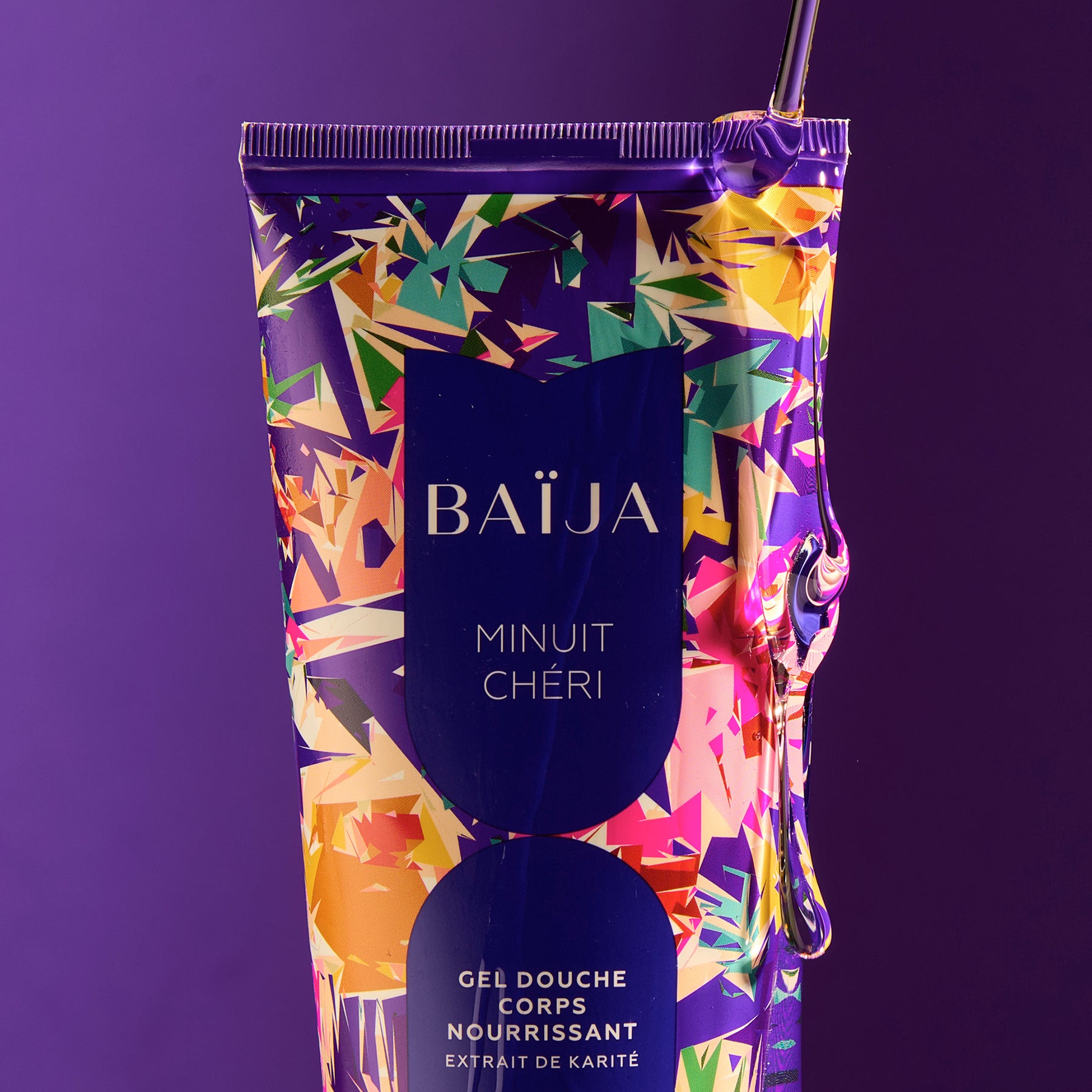 Gros plan sur le gel douche corps nourrissant Minuit Chéri à l’extrait de karité, présenté sur un fond violet profond.  
Le gel douche coule sur le tube pour révéler sa texture soyeuse.