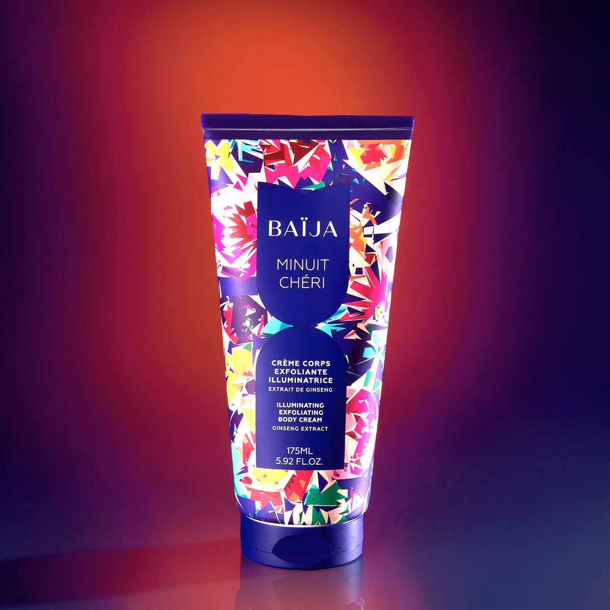 Tube de crème corps exfoliante illuminatrice Minuit Chéri à l’extrait de ginseng, sur fond dégradé violet et orangé.