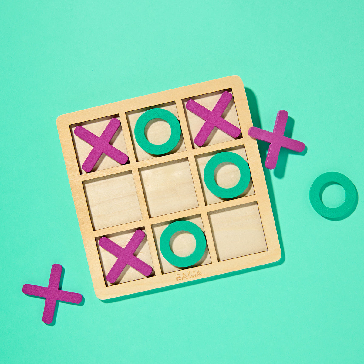 Jeu de morpion en bois BAÏJA avec pions violets et verts sur fond vert menthe, objet ludique et coloré provenant de la collection Moana.