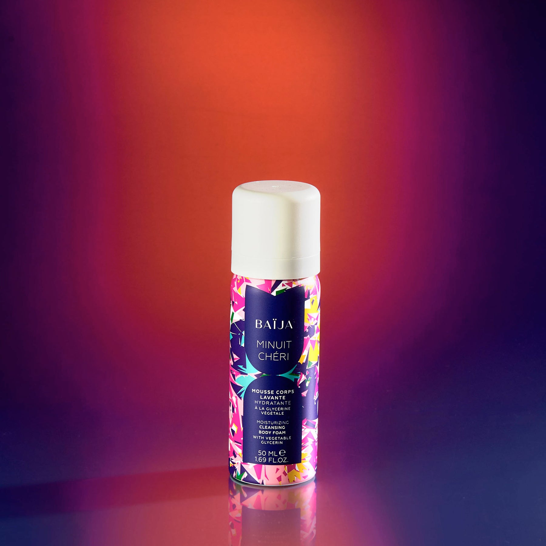 Mini mousse de douche Minuit Chéri, posé sur fond dégradé violet et orangé.