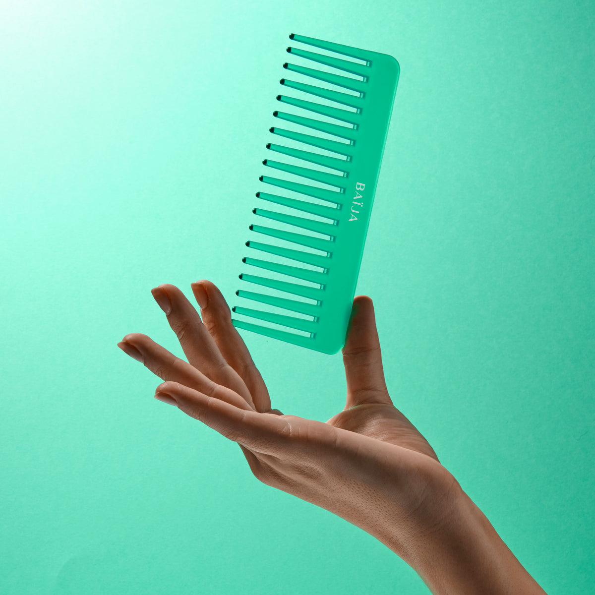 Peigne Baïja vert tenu entre les doigts sur fond vert pastel.