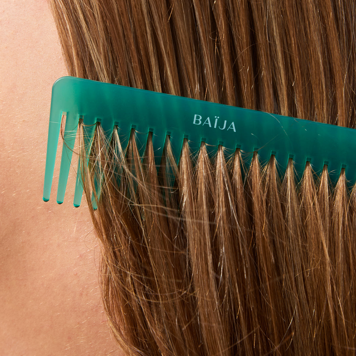 Peigne vert BAÏJA glissant dans des cheveux blonds, gros plan sur la texture brillante et soyeuse.