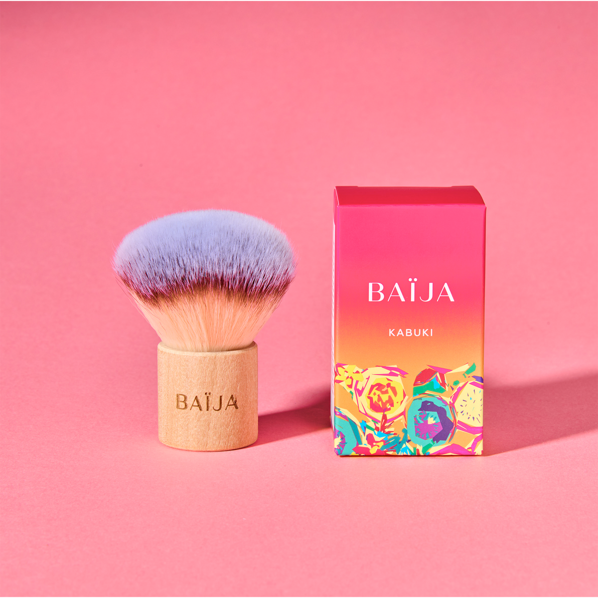 Pinceau Kabuki Baïja en bois et poils violets présenté à côté de sa boîte aux motifs floraux.
