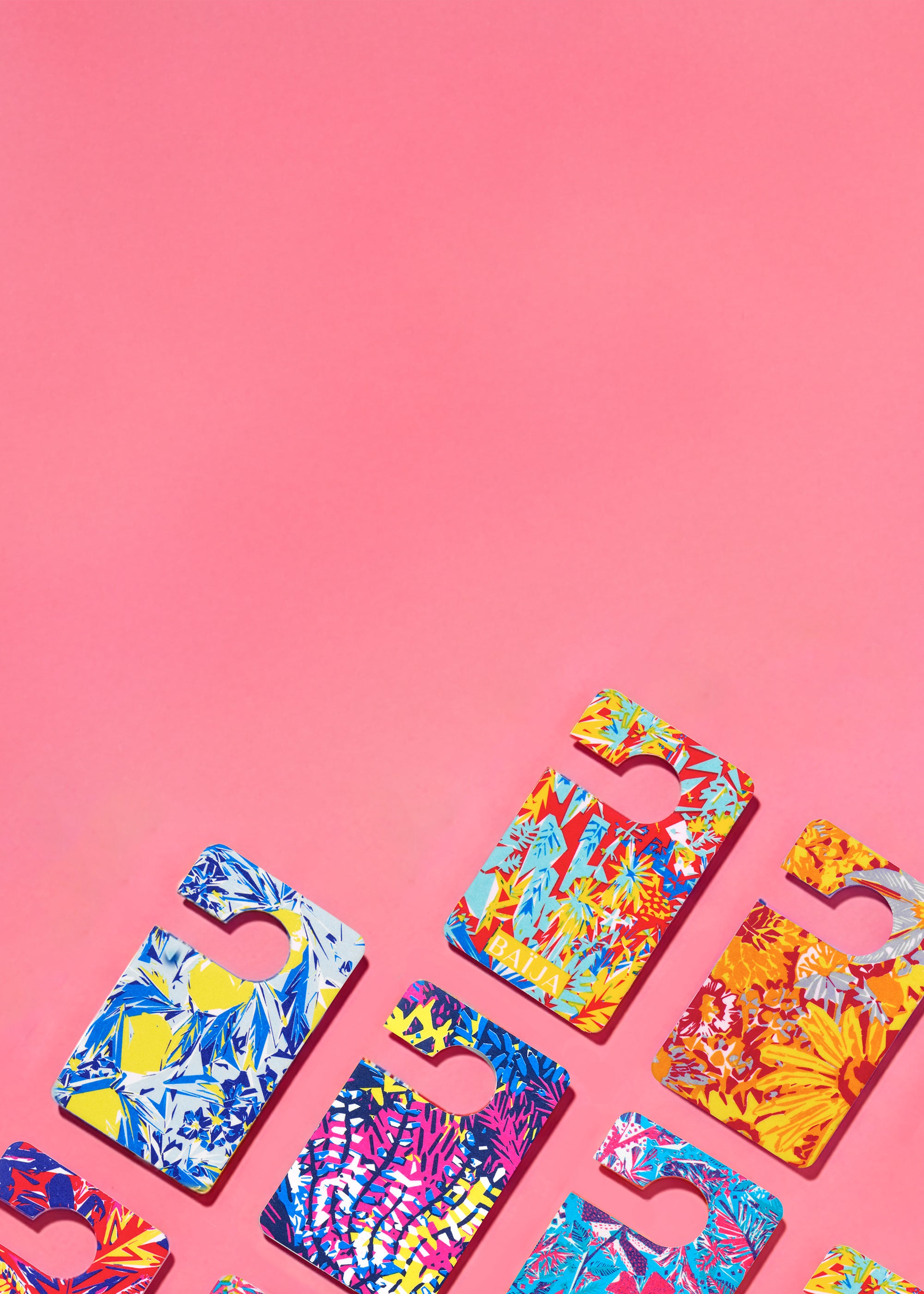 Flatlay de cartes de parfums voiture Baïja aux imprimés tropicaux et graphiques, disposées en diagonale sur un fond rose uni.