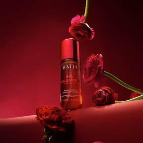 Flacon Baïja Bal Valentino brume parfumée, posé sur un décor rouge avec fleurs rouges en suspension et au premier plan, lumière chaude.