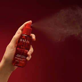 Main tenant le spray Baïja Bal Valentino et diffusant une fine brume dans l’air, fond rouge sombre et dégradé.