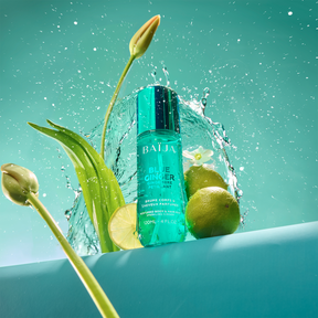 Flacon Baïja Blue Ginger entouré d’éclaboussures d’eau, feuilles vertes et citron vert coupé, ambiance fraîche sur fond lagon.