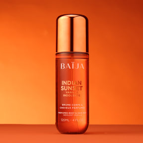 Packshot de la brume Baïja Indian Sunset (120 ml), flacon ambré orange avec capot métallisé cuivré, sur fond orange dégradé.