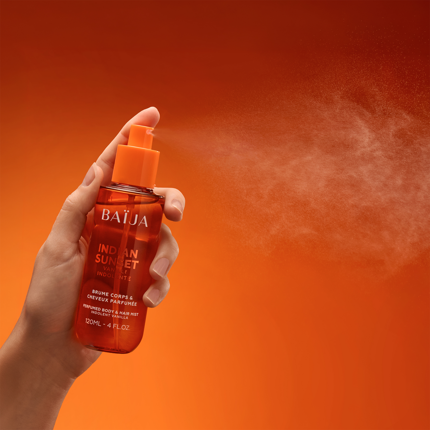 Main tenant le spray Baïja Indian Sunset et diffusant une fine brume dans l’air, ambiance orange chaude façon coucher de soleil.