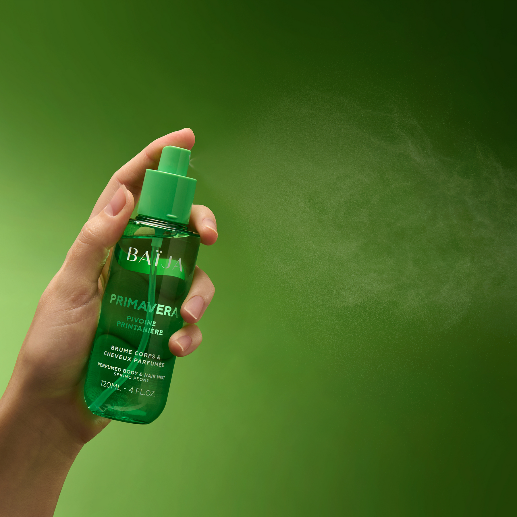 Main tenant le spray Baïja Primavera et diffusant une fine brume dans l’air, décor vert profond et printanier.