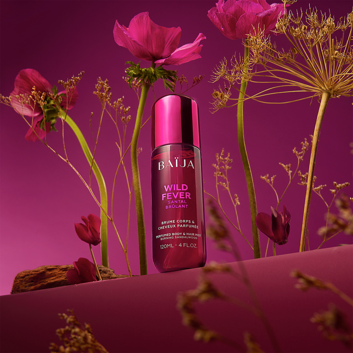 Flacon Baïja Wild Fever brume parfumée corps et cheveux, posé sur un décor violet avec fleurs pourpres et herbes sèches autour.