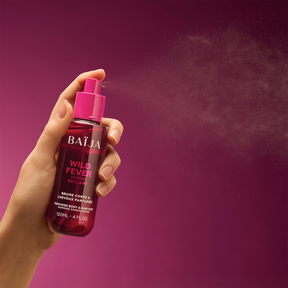 Main tenant le spray Baïja Wild Fever et diffusant une fine brume dans l’air, fond violet sombre et lumineux.