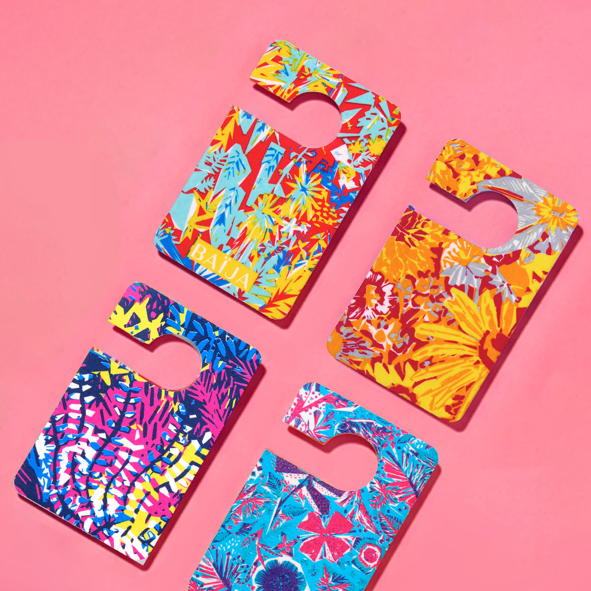 Flatlay de cartes de parfums voiture Baïja aux imprimés tropicaux et graphiques, disposées en diagonale sur un fond rose uni.