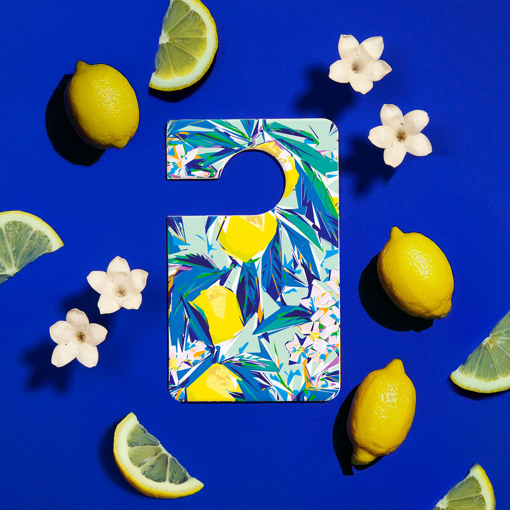 Parfum voiture Blue Ginger entouré de citrons et fleurs blanches. 