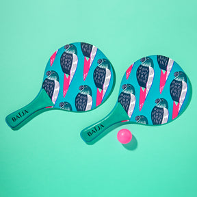 Deux raquettes de plage aux motifs d’oiseaux tropicaux bleus et roses avec balle rose, sur fond vert menthe, provenant de la collection Moana. 