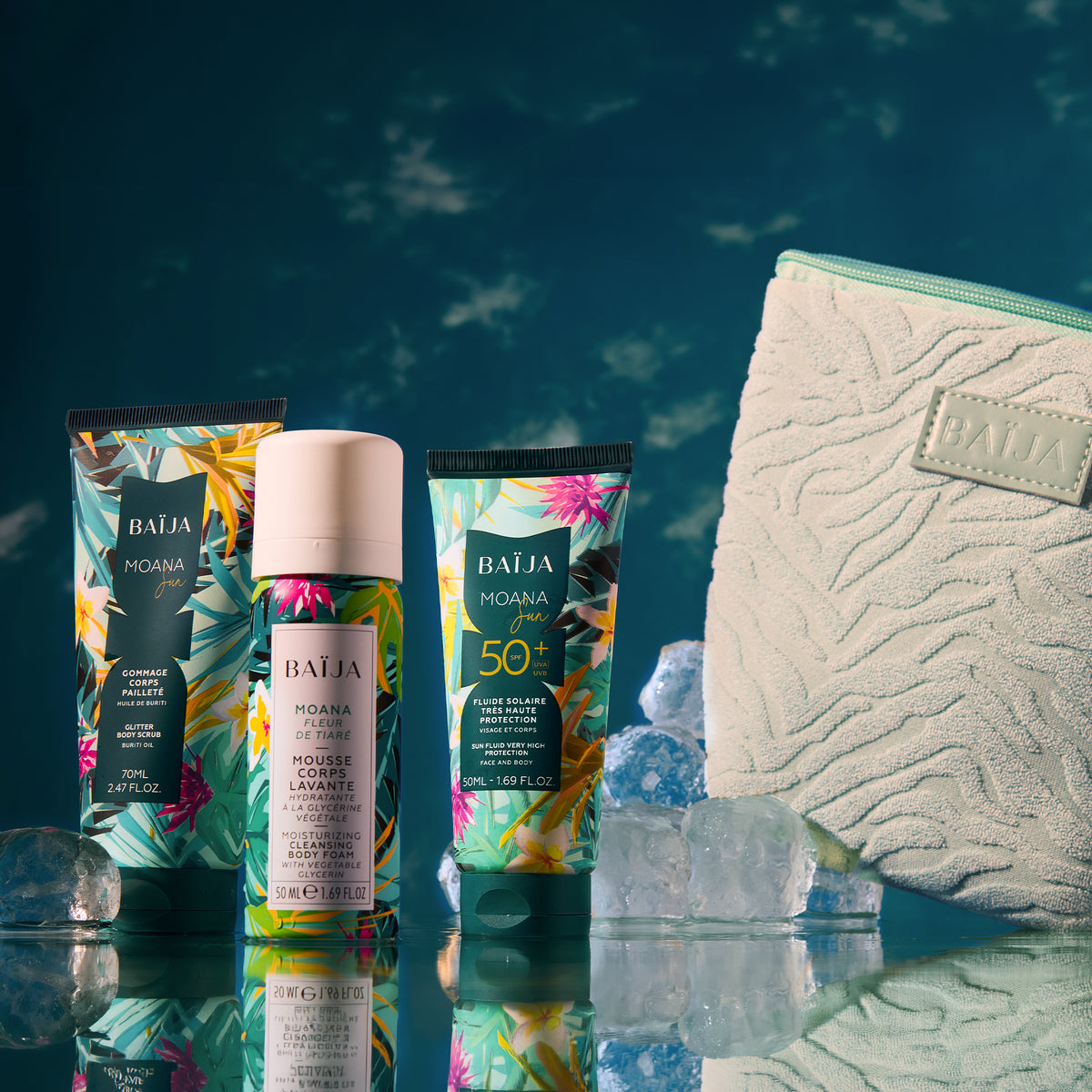 Packshot sur décor bleu profond : trois produits BAÏJA “Moana” (un tube gommage, une mousse corps en flacon, un tube solaire SPF 50+) posés sur un support brillant avec reflets. Des blocs de glace entourent les produits. À droite, une grande trousse vert menthe texturée avec logo “BAÏJA”. Éclairage studio, ambiance fraîche/estivale.