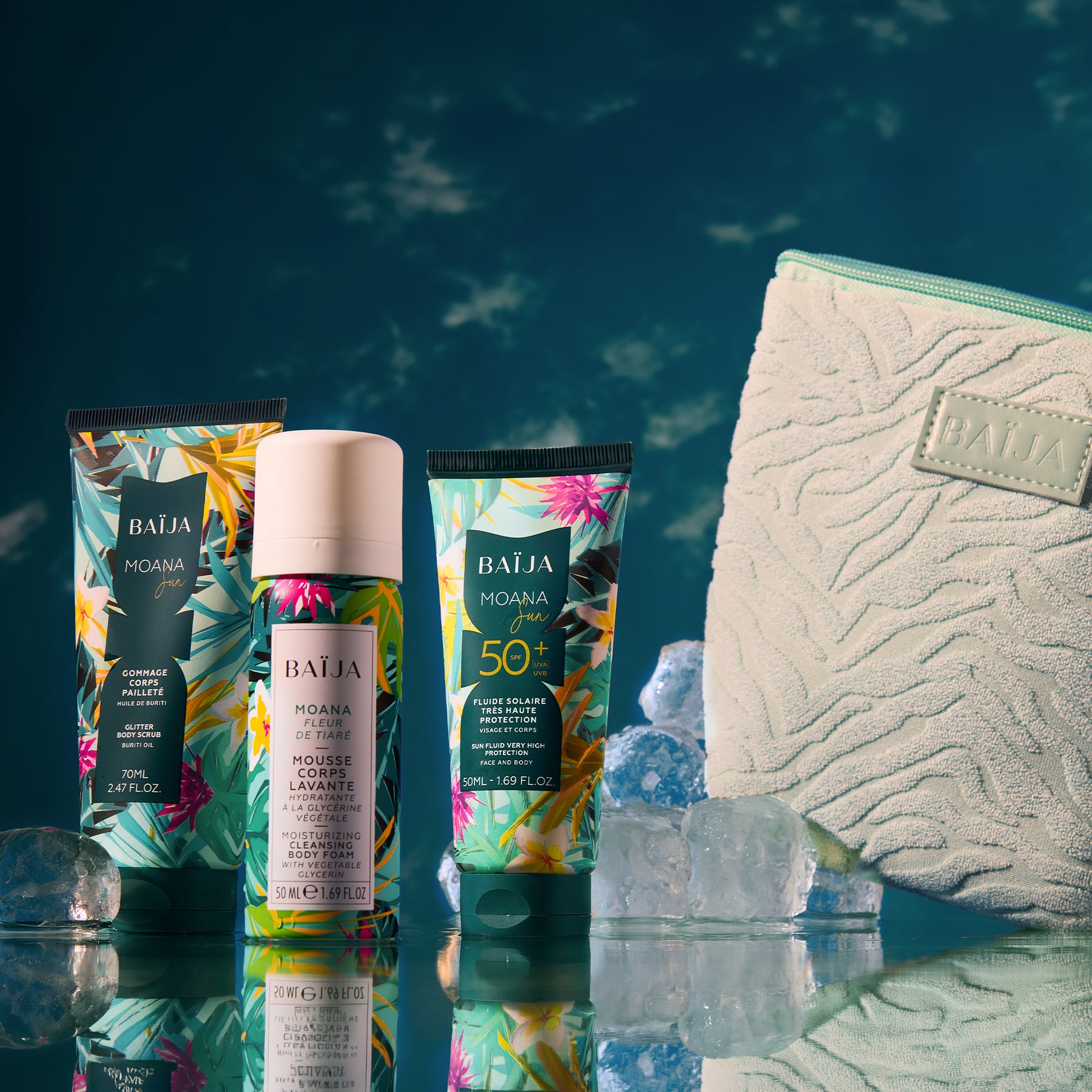 Packshot sur décor bleu profond : trois produits BAÏJA “Moana” (un tube gommage, une mousse corps en flacon, un tube solaire SPF 50+) posés sur un support brillant avec reflets. Des blocs de glace entourent les produits. À droite, une grande trousse vert menthe texturée avec logo “BAÏJA”. Éclairage studio, ambiance fraîche/estivale.