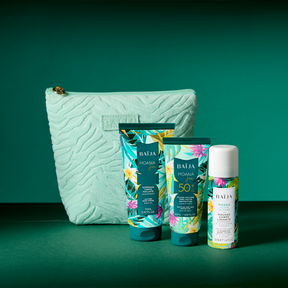 Packshot sur décor bleu profond : trois produits BAÏJA “Moana” (un tube gommage, une mousse corps en flacon, un tube solaire SPF 50+) posés sur un support brillant avec reflets. Des blocs de glace entourent les produits. À droite, une grande trousse vert menthe texturée avec logo “BAÏJA”. Éclairage studio, ambiance fraîche/estivale.