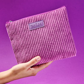 Trousse en velours côtelé violet tenue à la main sur fond mauve, accessoire doux et élégant de la collection minuit chéri. 