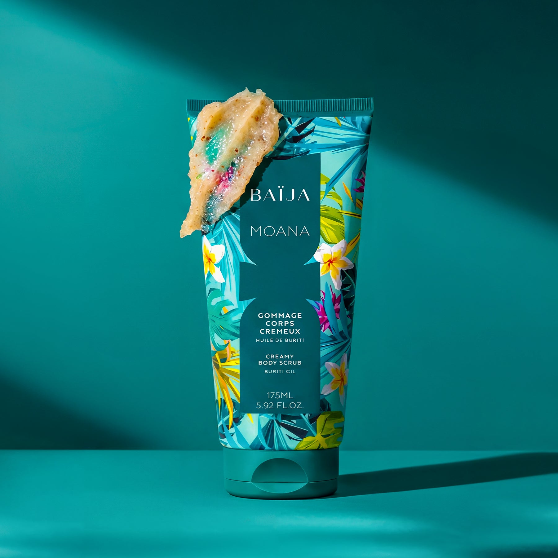 Tube de gommage corps crémeux Baïja Moana à l’huile de buriti, surmonté de sa texture exfoliante, dans une ambiance inspirée des lagons tropicaux.