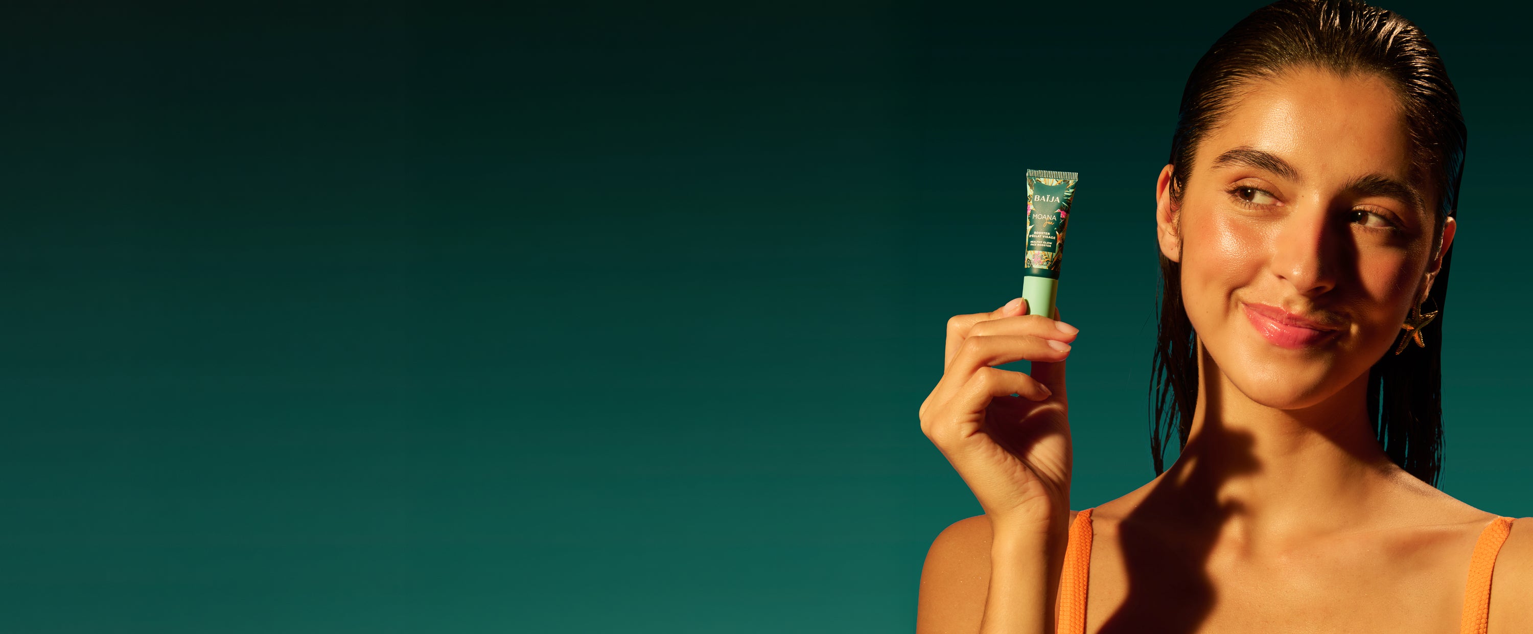 Portrait d’une femme en maillot corail tenant le booster éclat visage Moana Baïja, soin illuminateur au parfum fleur de tiaré dans une ambiance solaire et estivale.