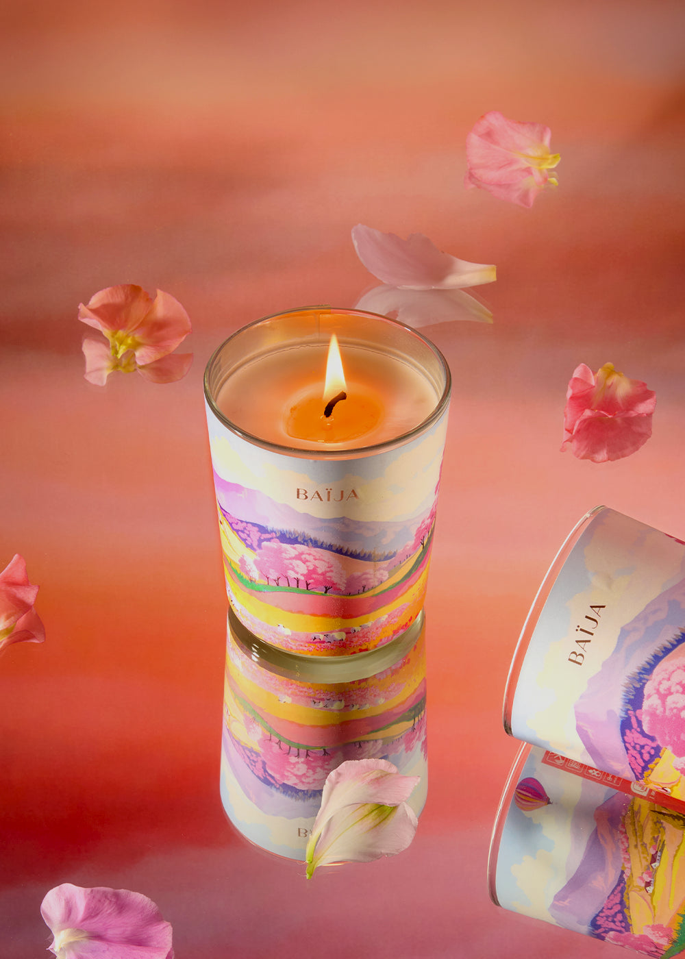 Bougie parfumée Sweet Sunday Baïja avec son écrin illustré, entourée de pétales roses sur fond corail, évoquant un moment de bien-être réconfortant.