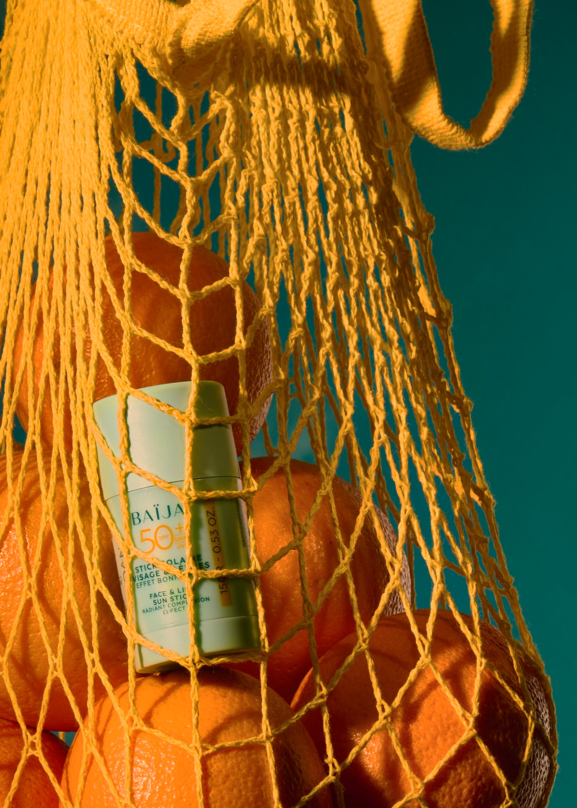 Stick solaire SPF50+ Baïja dans un filet d’oranges, scène estivale colorée inspirant protection solaire et éclat naturel en vacances.