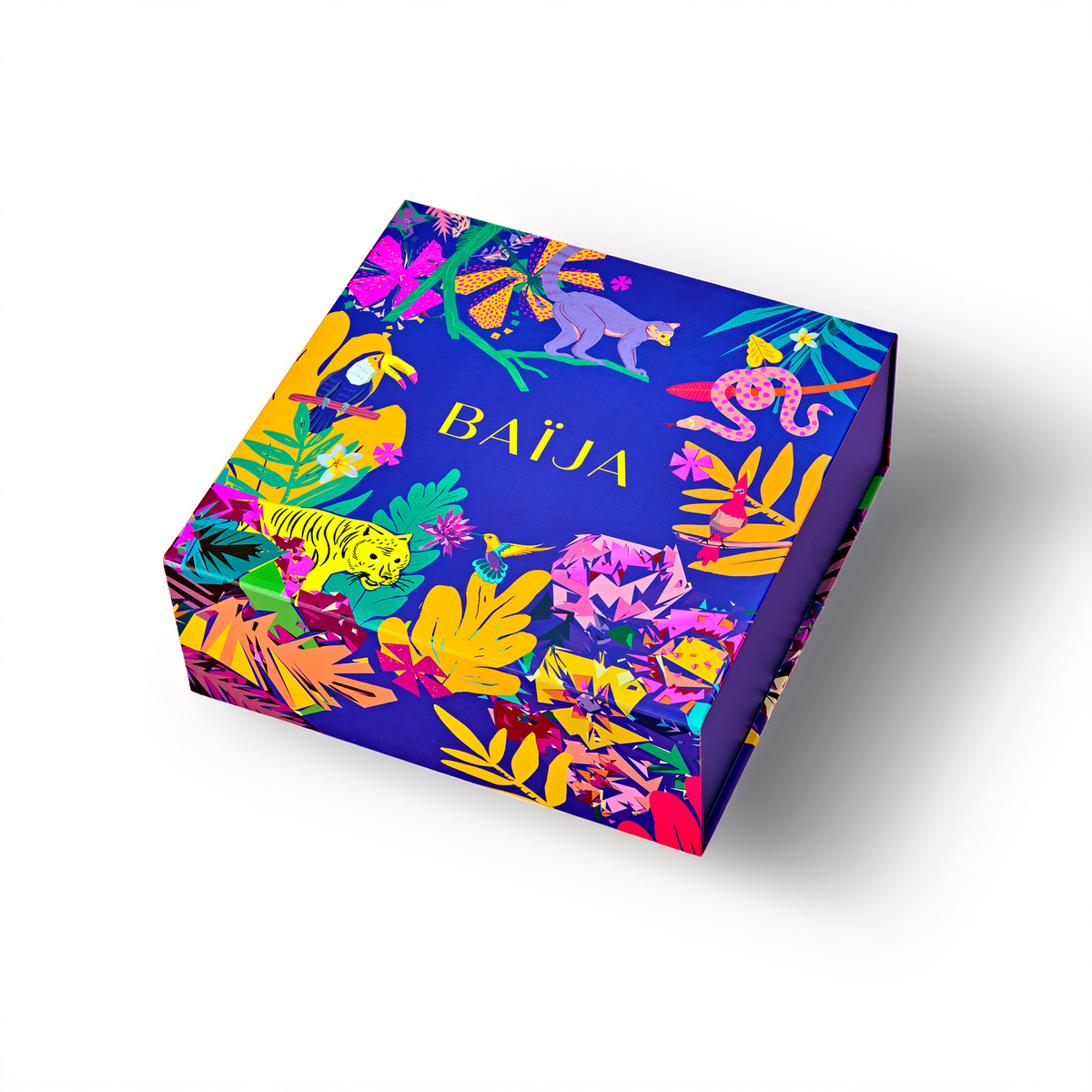 Packshot d'une boîte coffret cadeau Baïja fermée, présentée en perspective sur fond blanc. Son packaging bleu violet est orné d'illustrations tropicales aux couleurs éclatantes : fleurs exotiques roses et jaunes, feuillages luxuriants, tigre jaune, toucan, serpent et autres animaux sauvages. Le logo Baïja apparaît en lettres jaunes au centre du couvercle.