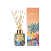 Bouquet parfumé Lost Paradise de Baïja, à la senteur d'ananas des Antipodes. Ce diffuseur de parfum d'intérieur se présente dans un flacon en verre cylindrique décoré d'un paysage tropical aux nuances orangées, bleues et vertes, avec un col doré et des bâtonnets diffuseurs en bois naturel. À ses côtés, un coffret aux dégradés orangés et rosés illustre un paysage exotique avec des palmiers, des oiseaux, un félin tacheté et un coucher de soleil. L'ensemble est photographié de face sur fond blanc.