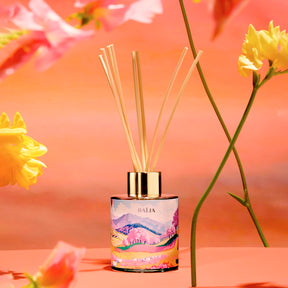 Diffuseur de parfum d’intérieur Baïja Sweet Sunday mis en scène parmi des fleurs pastel sur fond rose chaleureux.