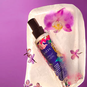 Brume corps parfumée hydratante Baïja Minuit Chéri posée sur un bloc de glace, entourée d’orchidées violettes.