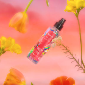 Brume parfumée apaisante Sweet Sunday flottant parmi des fleurs colorées, symbole de fraîcheur et de douceur.