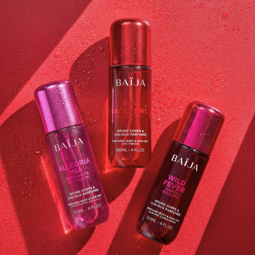 Packshot créatif de trois brumes corps et cheveux parfumées Baïja (Allegra Mia, Bal Valentino et Wild Fever) disposées sur un fond rouge texturé avec gouttelettes d'eau et jeux de lumière, illustrant la collection de brumes parfumées.