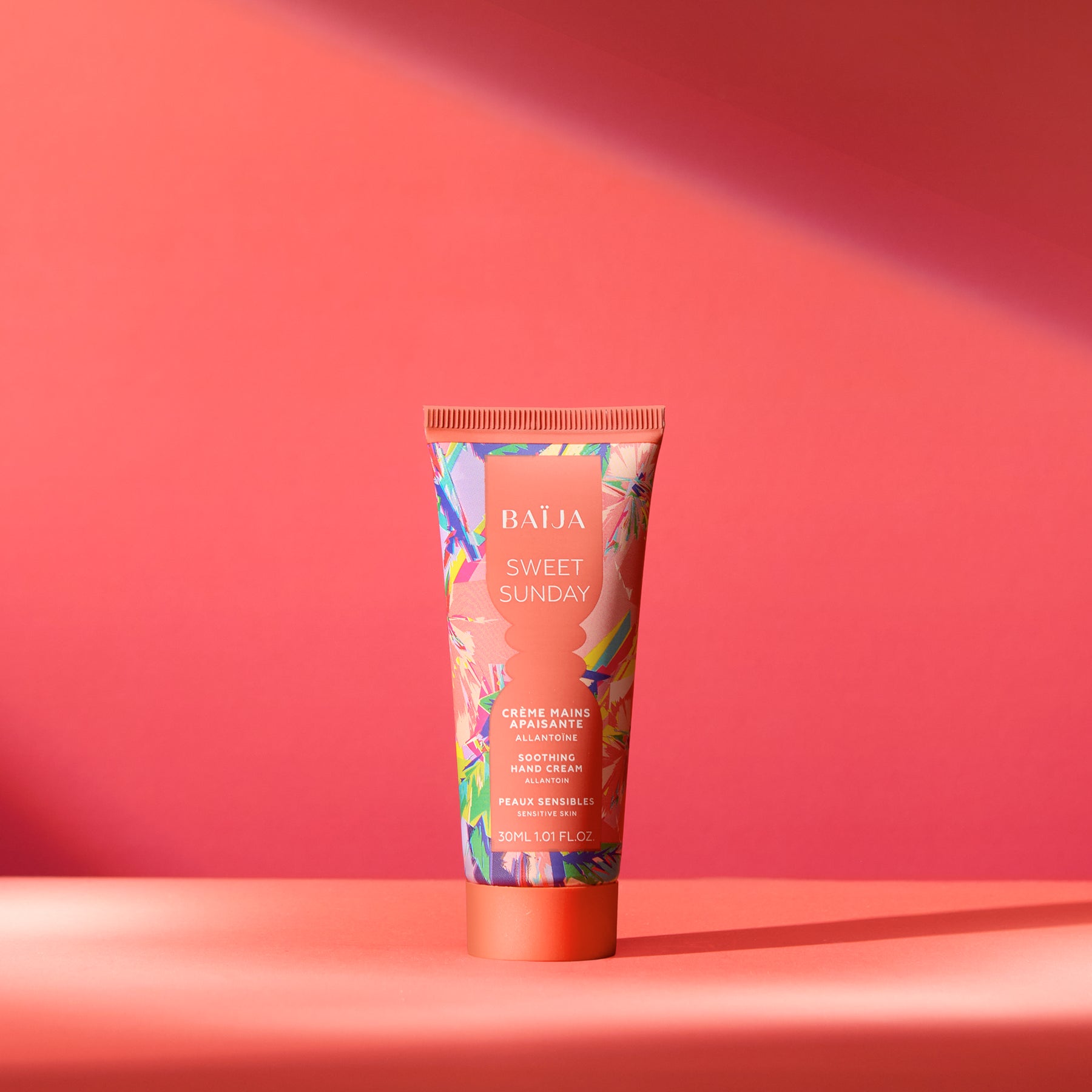 Tube de crème mains Sweet Sunday Baïja présenté dans une ambiance solaire aux nuances corail et rose