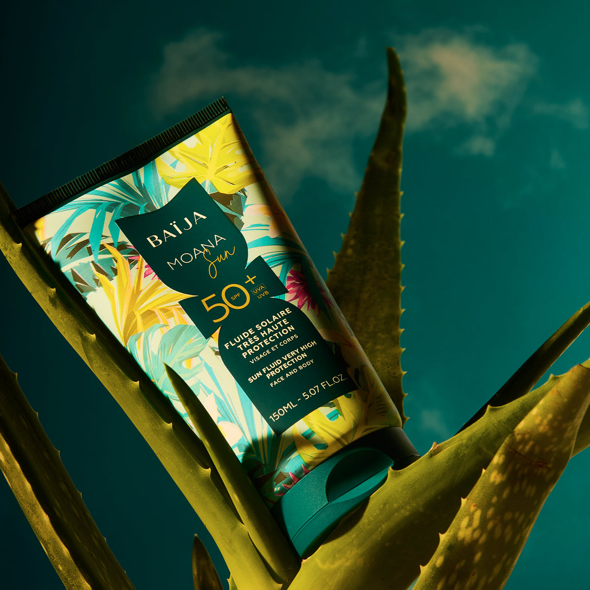 Tube de fluide solaire SPF50+ Baïja Moana Sun sur feuilles d’aloe vera, évoquant fraîcheur, protection UVA UVB et soin corps naturel