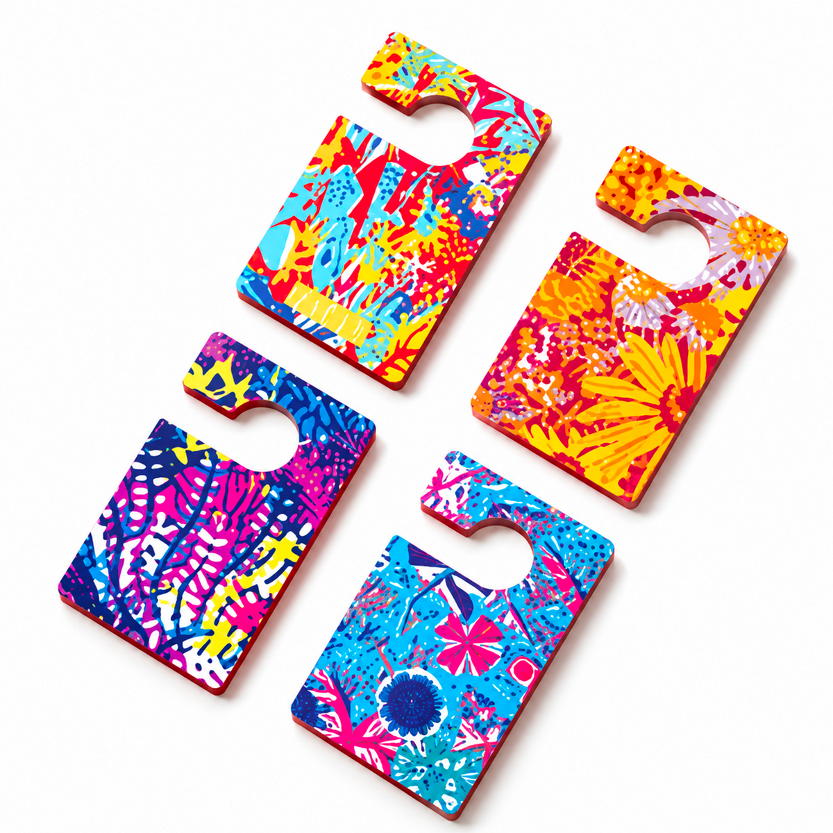 Packshot de quatre diffuseurs de parfum pour voiture Baïja, de forme rectangulaire avec encoche de fixation, aux motifs floraux et tropicaux colorés. Présentés à plat, ils se déclinent dans des teintes vives de bleu, rose, jaune et orange.