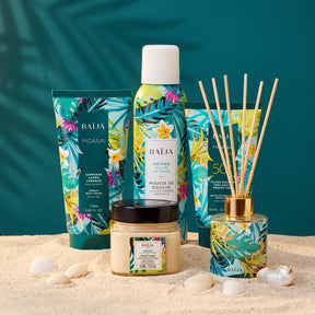 Rituel Baïja Moana mis en scène sur le sable avec gommage corps, mousse de douche, crème corps, fluide solaire SPF50+ et diffuseur de parfum d’ambiance.