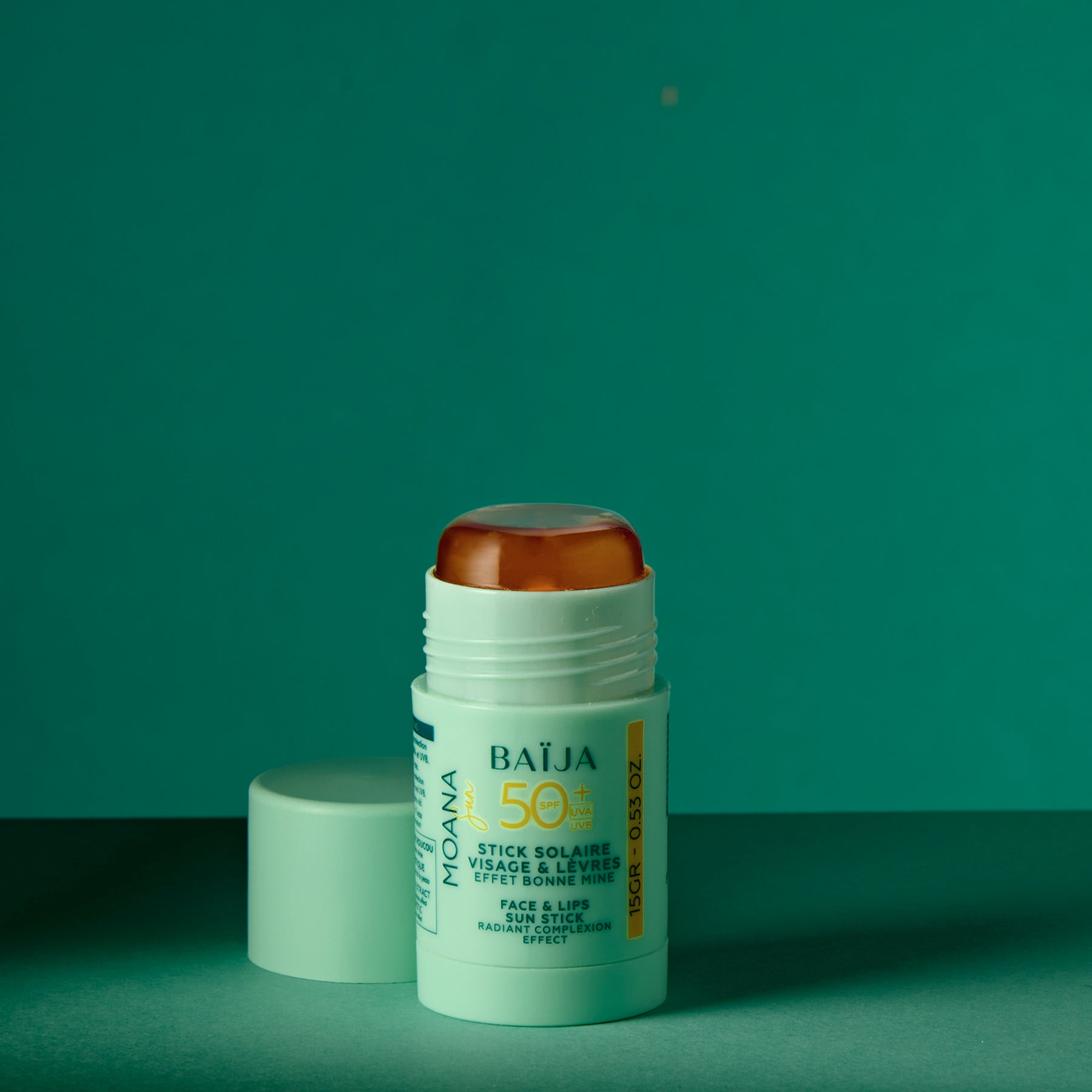 Photo produit/packshot d’un stick solaire “BAÏJA” vert menthe, présenté verticalement, bouchon ambré translucide visible (ou partiellement visible selon le cadrage). Fond clair/uni, rendu très net type e-commerce.