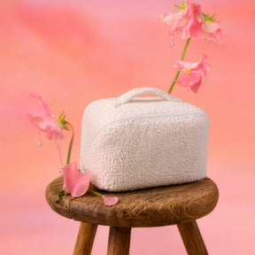 Vanity Sweet Sunday en bouclette écrue posé sur un tabouret en bois parmi des fleurs roses